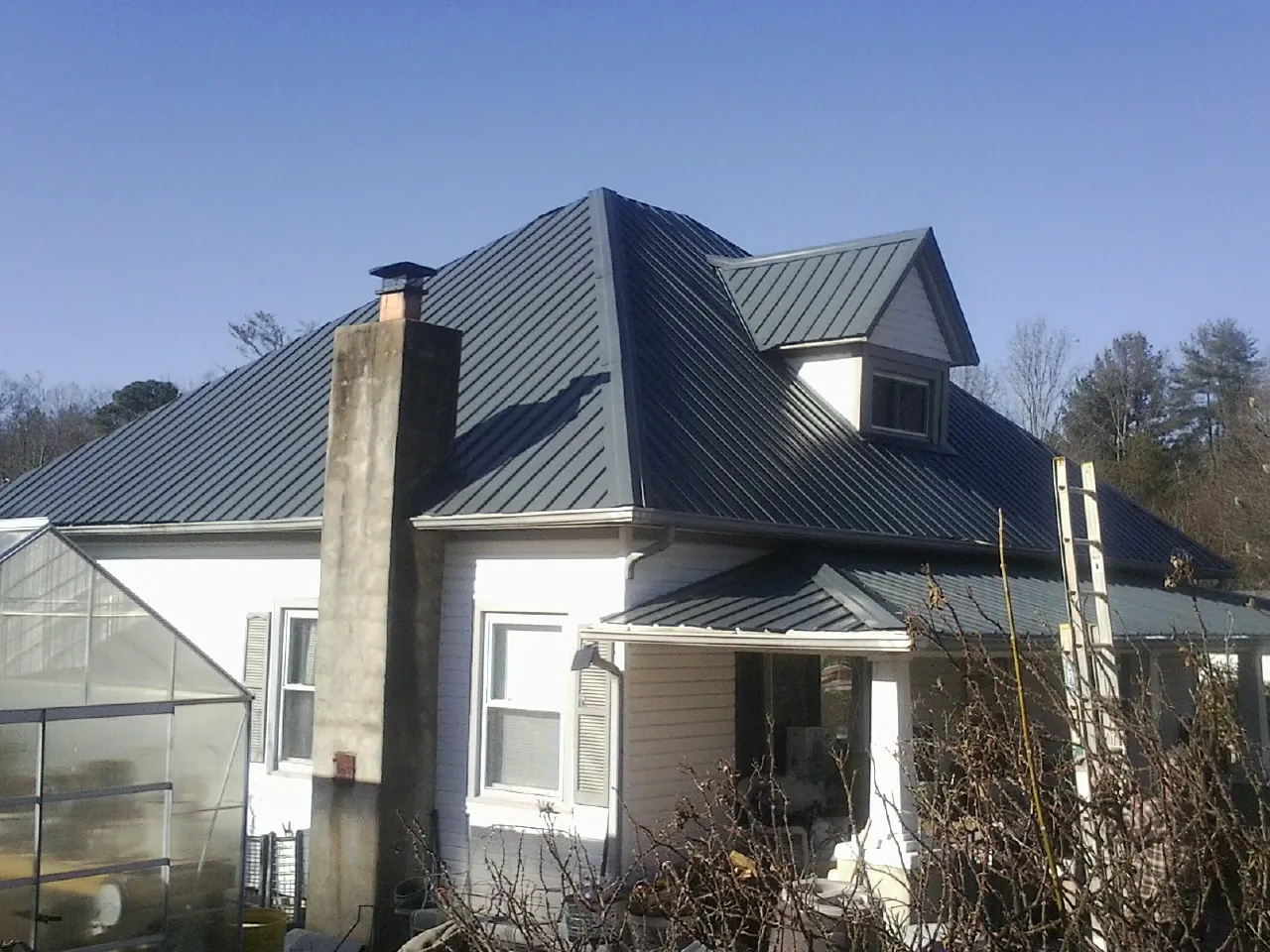 Dark blue standing seam metal roof on a white farmhouse with dormer — Slate & Tile Roof Repair by Roofing Brothers in Terry