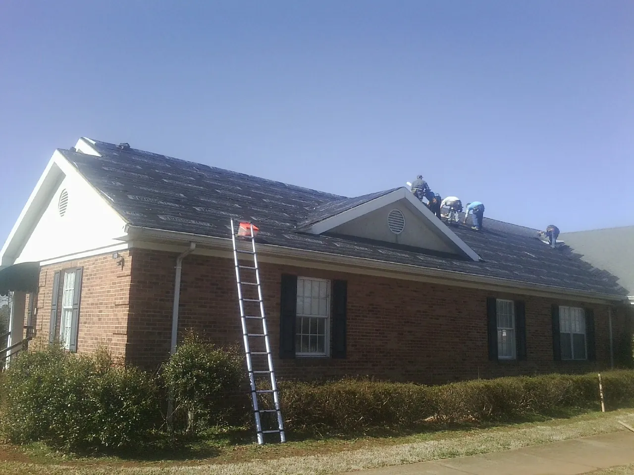 Crew tearing shingles off a brick ranch roof with a ladder set — Emergency Roof Repair work by our crew in Terry