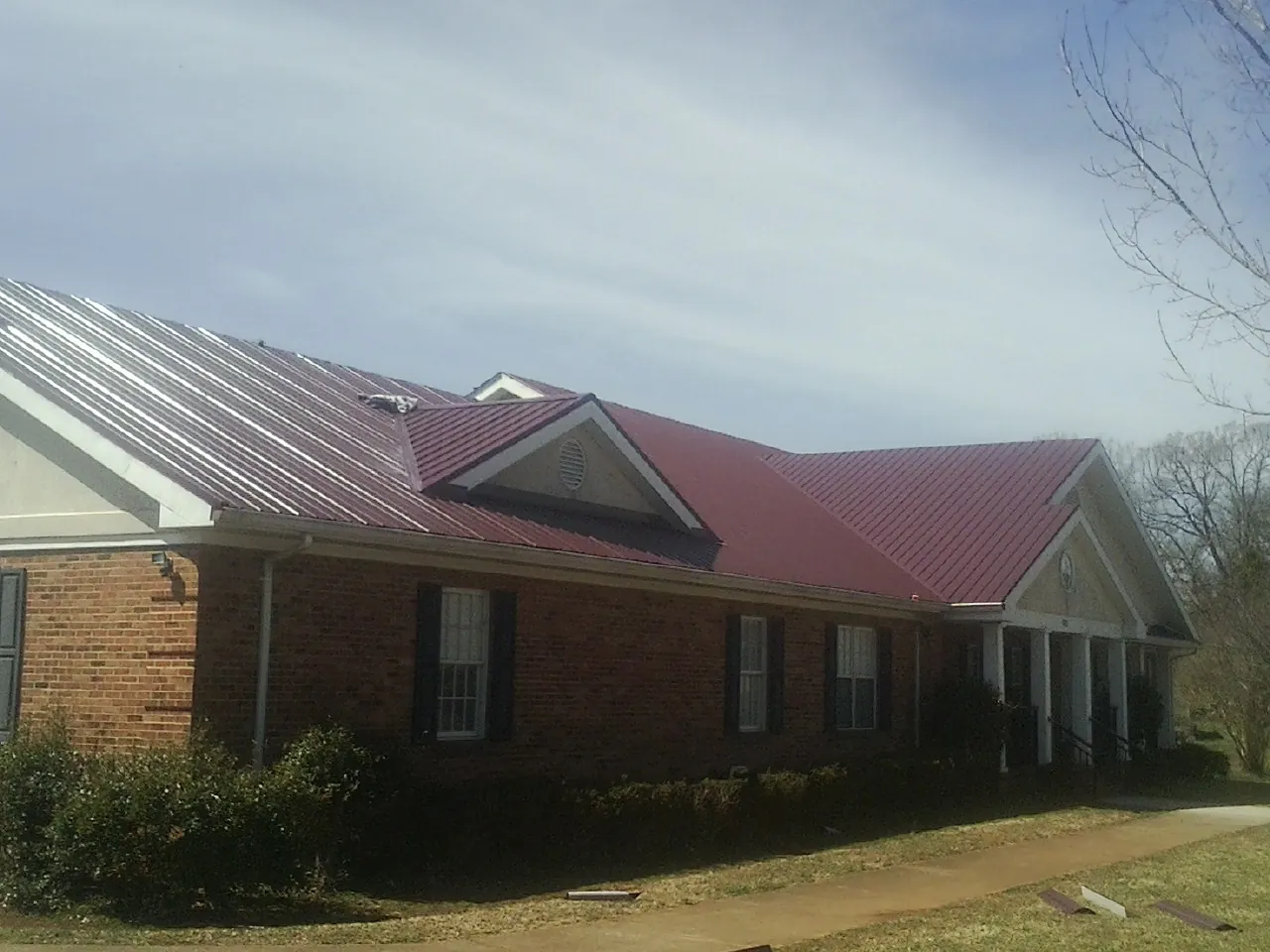 Red metal roof with gabled entries on a long brick building, from a Hail Damage Roof Repair job in Terry