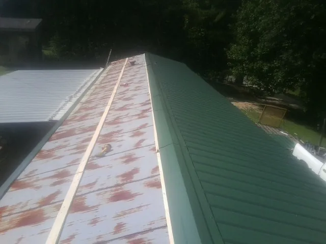 Old rusted panels beside newly installed green metal roofing — Wind Damage Roof Repair by Roofing Brothers in Terry