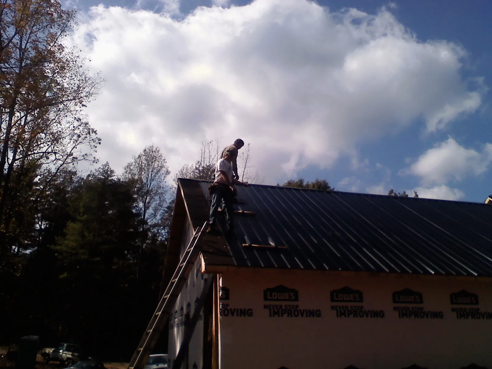 Roofer fastening dark metal panels high against a cloudy sky, from a Roof Inspection job in Terry